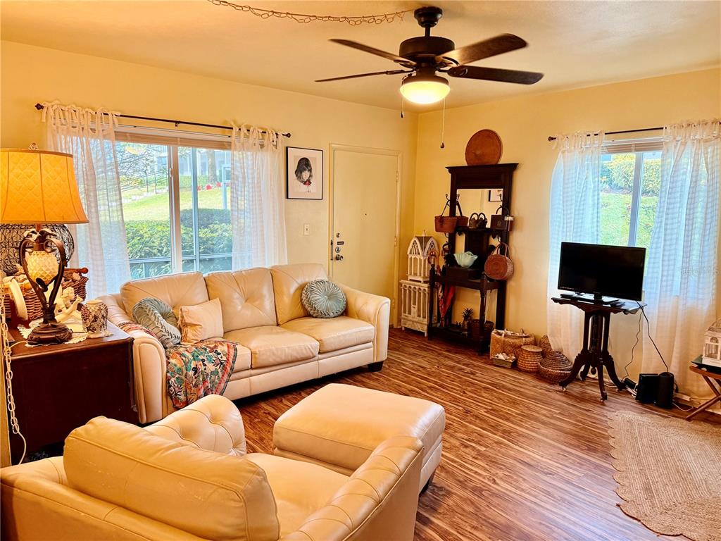 A living room features a beige sofa, matching ottoman, wood-look flooring, and a ceiling fan — 1700 6TH STREET NW UNIT C1, WINTER HAVEN, FL