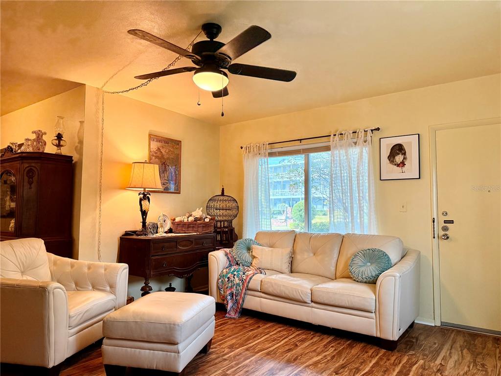 A living room features a white sofa, matching armchair, ottoman, ceiling fan, and wood flooring — 1700 6TH STREET NW UNIT C1, WINTER HAVEN, FL