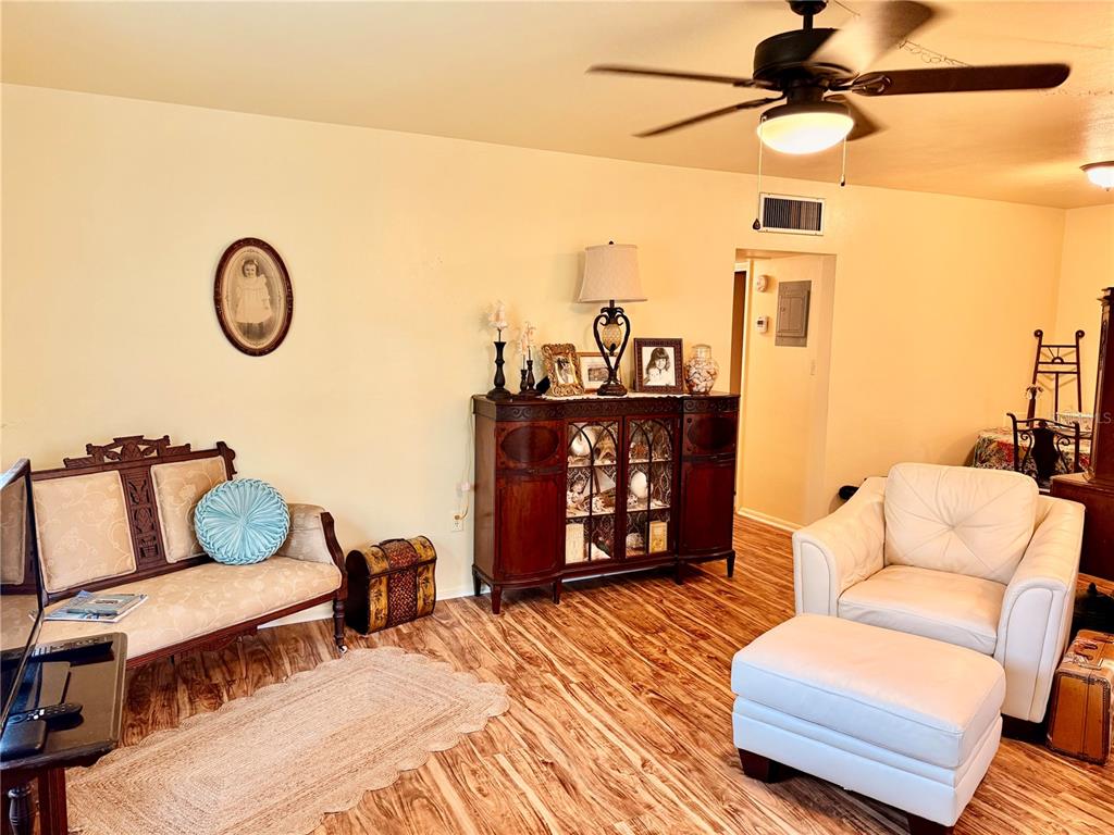 A living room features wood-look flooring, a ceiling fan, a settee, and a white armchair — 1700 6TH STREET NW UNIT C1, WINTER HAVEN, FL