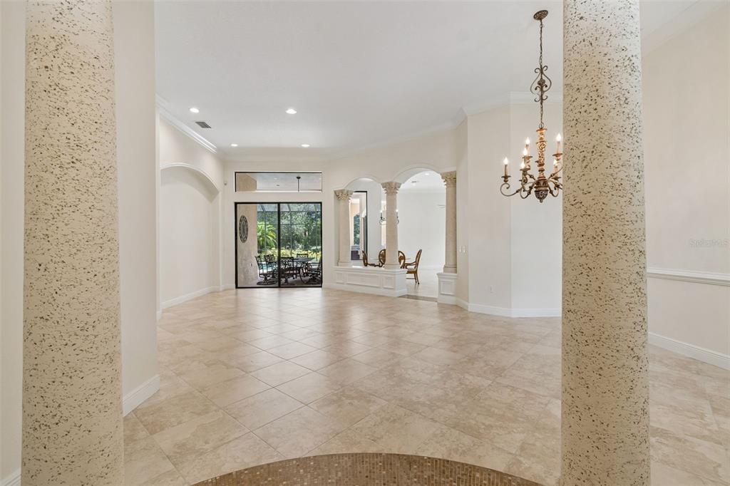 A spacious, tiled living area features decorative columns, a chandelier, and sliding glass doors — 7222 LAKE FOREST GLEN, BRADENTON, FL