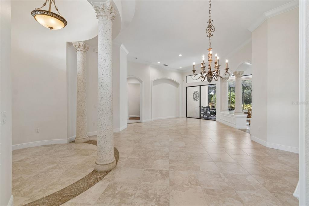 A spacious, light-filled room features tile flooring, decorative columns, and two ornate chandeliers — 7222 LAKE FOREST GLEN, BRADENTON, FL