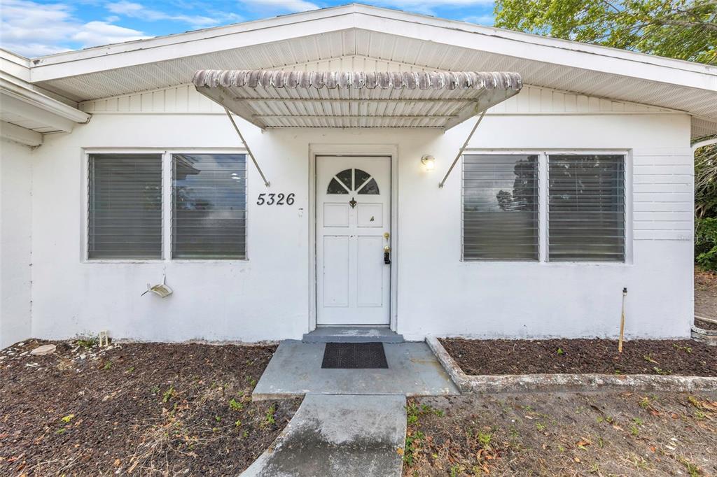 The exterior of a white house features a metal awning over the front entrance door — 5326 BERKLEY ROAD, NEW PORT RICHEY, FL