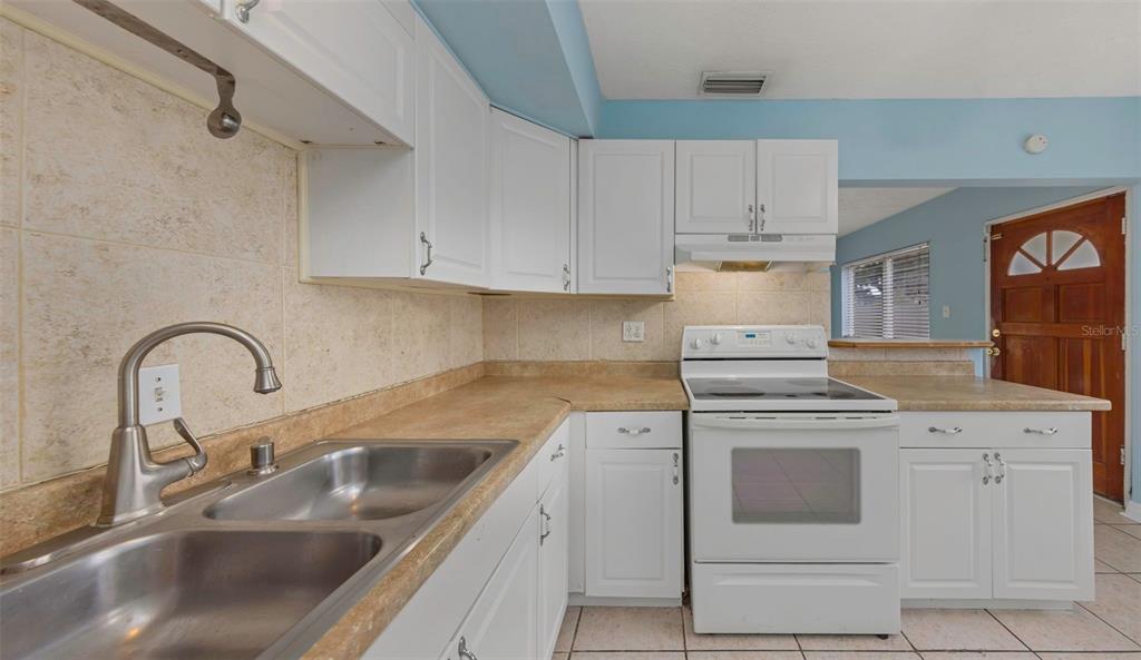 A kitchen features white cabinets, a double sink, a white stove, and light-colored countertops — 5326 BERKLEY ROAD, NEW PORT RICHEY, FL