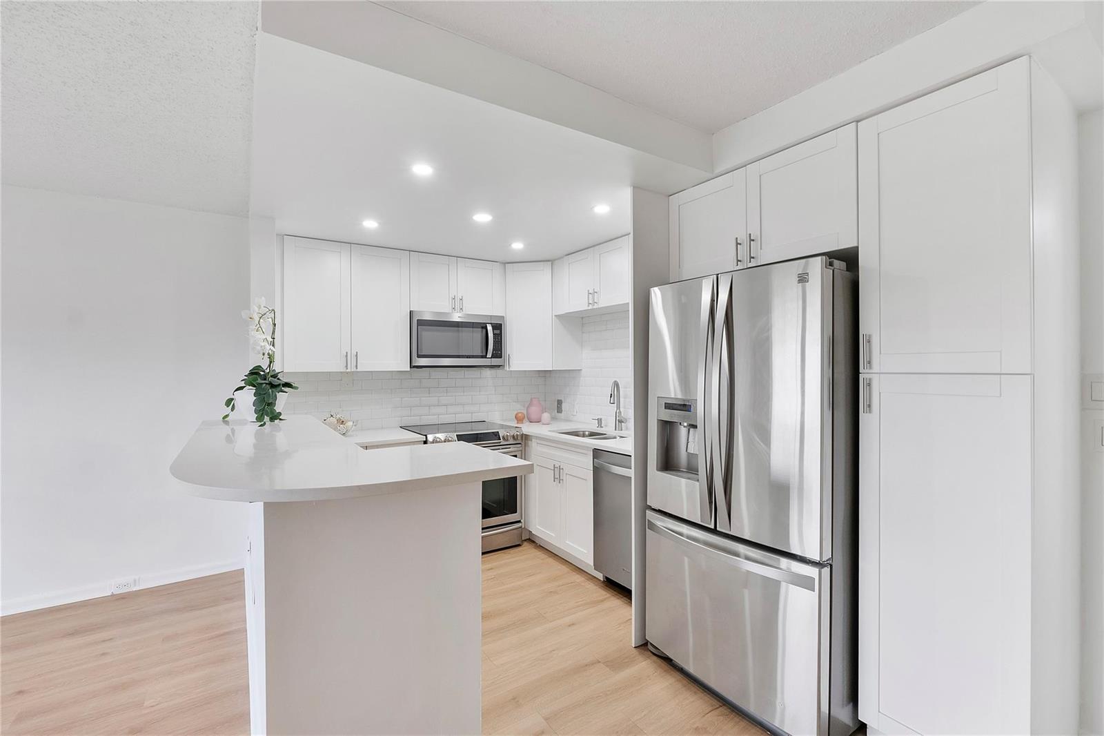 A modern kitchen features white cabinets, stainless steel appliances, and a peninsula with quartz countertops — 457 Mansfield # 457, Boca Raton FL 33434, BOCA RATON, FL