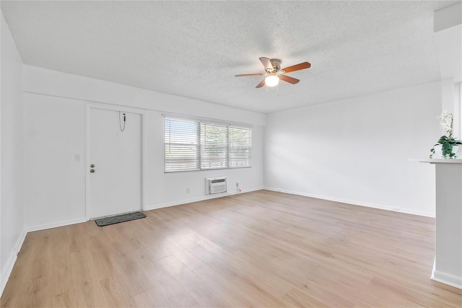 An empty living room features light wood-look flooring, white walls, a ceiling fan, and windows — 457 Mansfield # 457, Boca Raton FL 33434, BOCA RATON, FL
