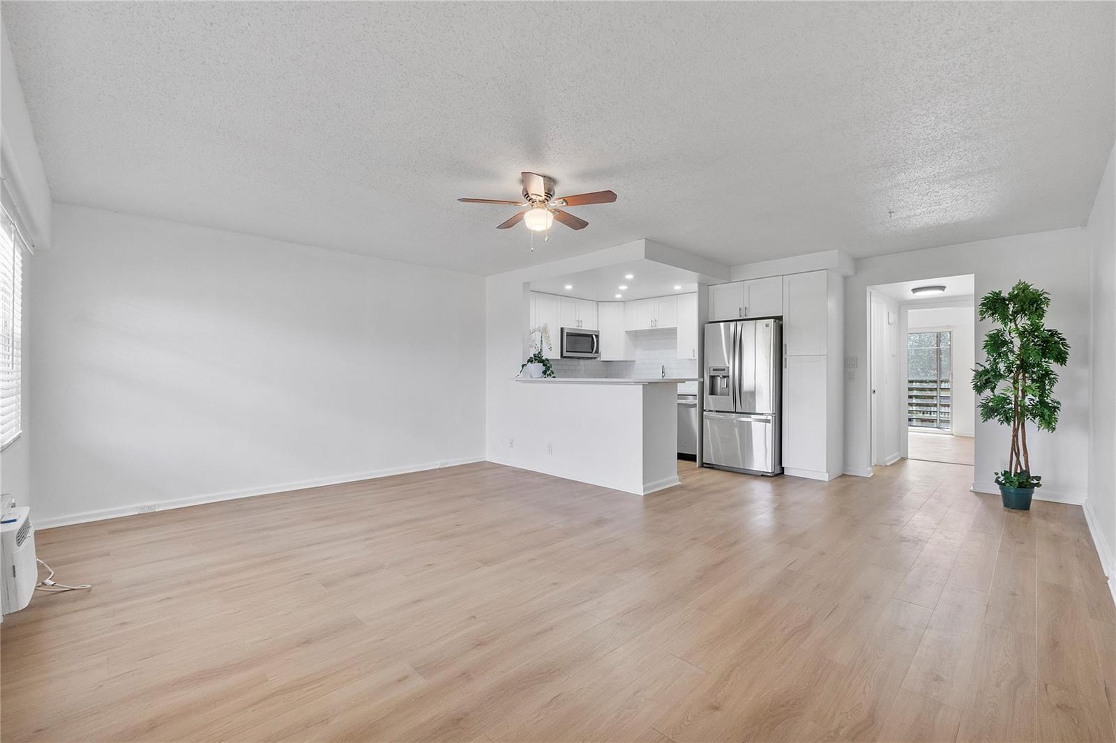 An open-concept living room features light wood flooring, white walls, and an adjacent kitchen — 457 Mansfield # 457, Boca Raton FL 33434, BOCA RATON, FL