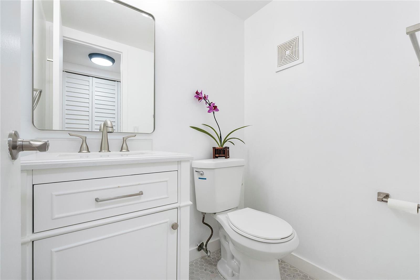 A small bathroom features a white vanity, a toilet, and a mirror on white walls — 457 Mansfield # 457, Boca Raton FL 33434, BOCA RATON, FL