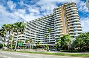 A multi-story residential building with curved balconies stands behind palm trees and a road — 5555 Collins Ave # 15W, Miami Beach FL 33140, MIAMI BEACH, FL