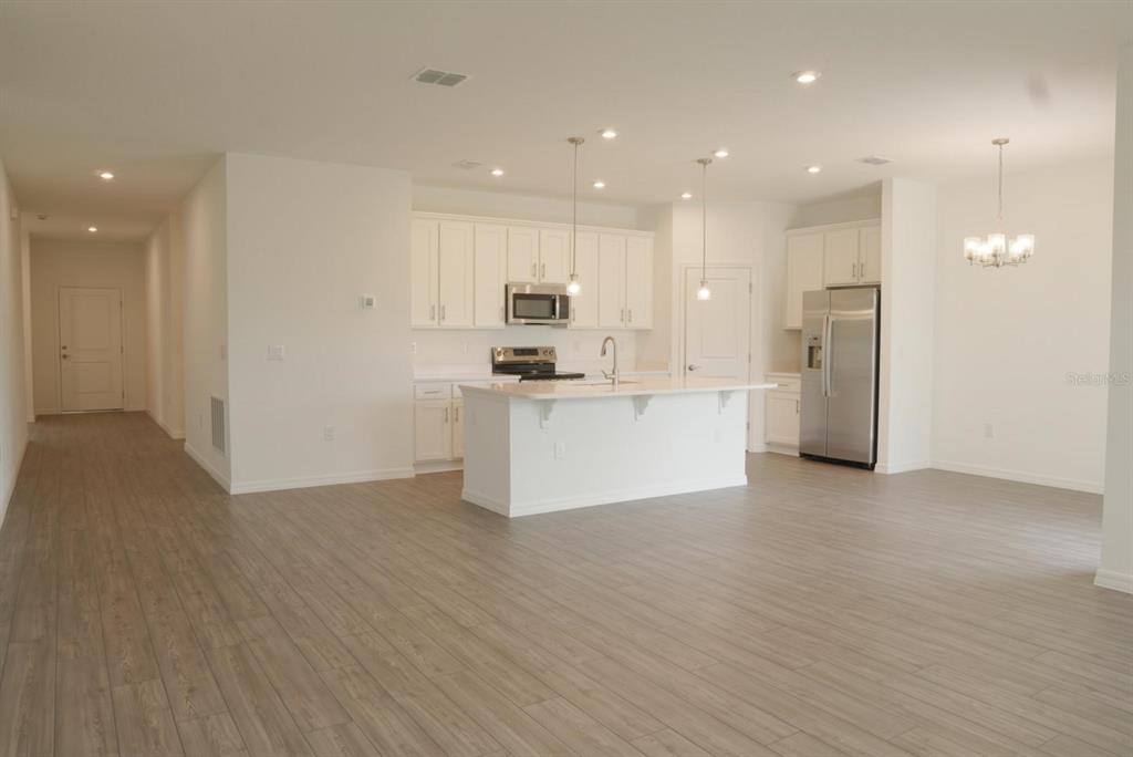 A bright, open-concept kitchen features white cabinetry, a center island, and light wood-look flooring — 1762 FLAG STREET, HAINES CITY, FL