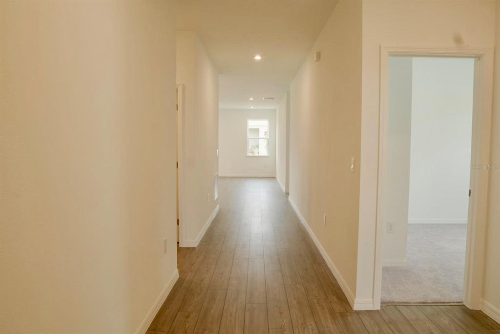 A hallway with light wood-look flooring leads to a room with a window — 1762 FLAG STREET, HAINES CITY, FL