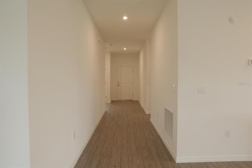 A hallway with light wood-look flooring leads to a white door at the end — 1762 FLAG STREET, HAINES CITY, FL