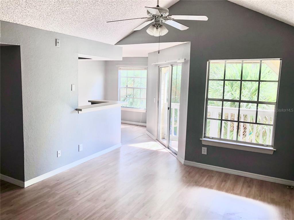 An empty living room features light wood flooring, a vaulted ceiling, and a sliding glass door — 1037 S HIAWASSEE ROAD UNIT 2835, ORLANDO, FL