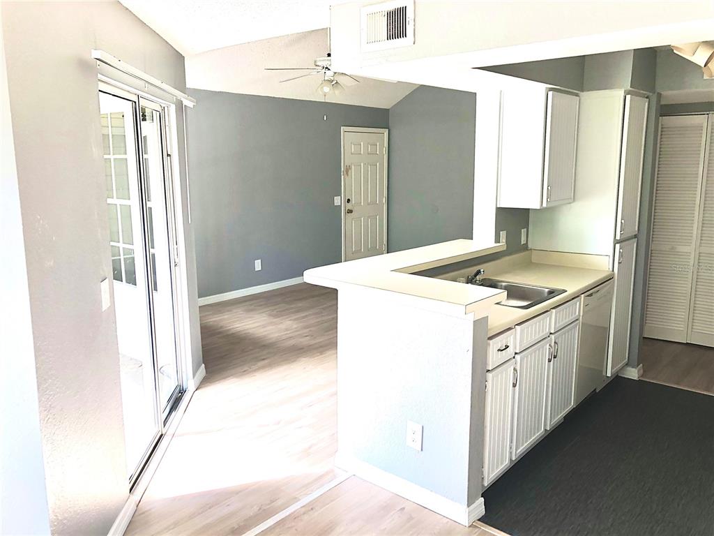 A kitchen with white cabinets and a breakfast bar overlooks a living area with gray walls — 1037 S HIAWASSEE ROAD UNIT 2835, ORLANDO, FL