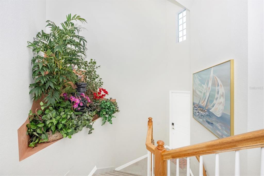 A staircase with a wooden railing leads to a landing featuring a built-in plant niche — 17770 BORACAY COURT UNIT 201, VENICE, FL