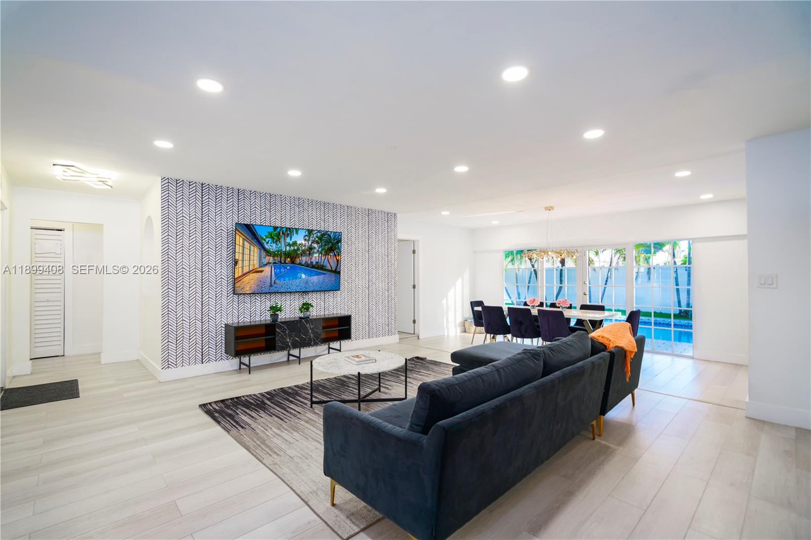 A living and dining area features a patterned accent wall, dark furniture, and pool views — 1244 Garfield St, Hollywood FL 33019, HOLLYWOOD, FL