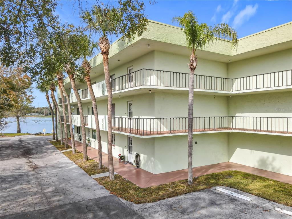 A three-story apartment building with exterior walkways and palm trees overlooks a lake — 1130 N LAKE PARKER AVENUE UNIT A302, LAKELAND, FL
