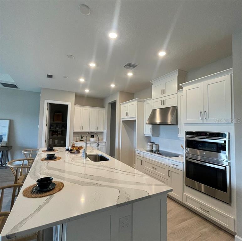 A modern kitchen features white cabinetry, a large marble-topped island, and stainless steel appliances — 5676 NEVIS TERRACE, KISSIMMEE, FL