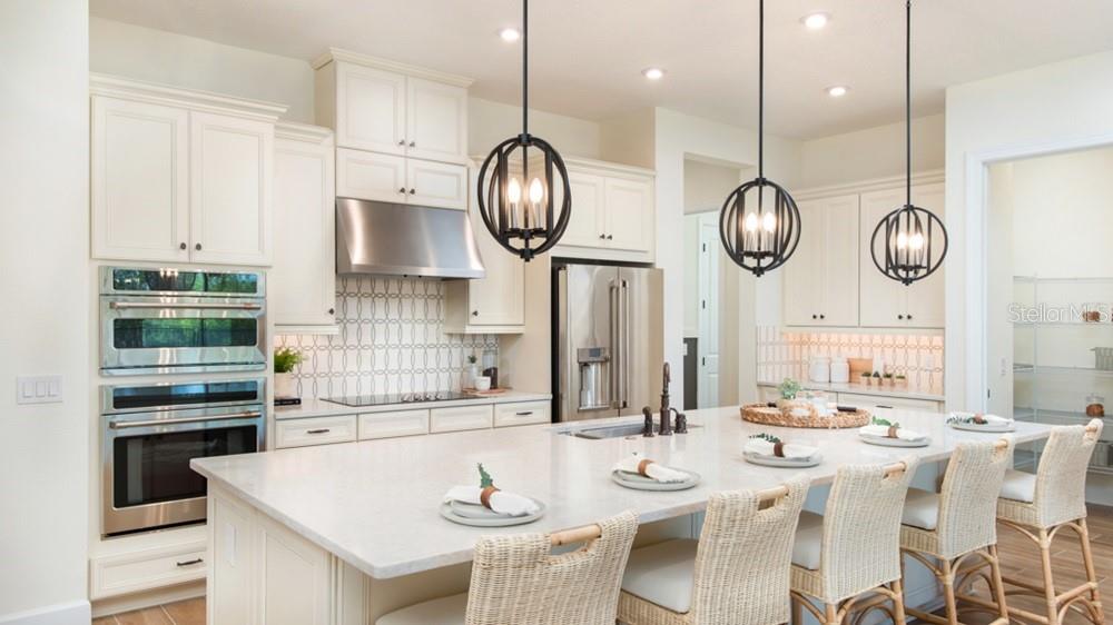 A kitchen features white cabinetry, stainless steel appliances, a large island, and three pendant lights — 5676 NEVIS TERRACE, KISSIMMEE, FL