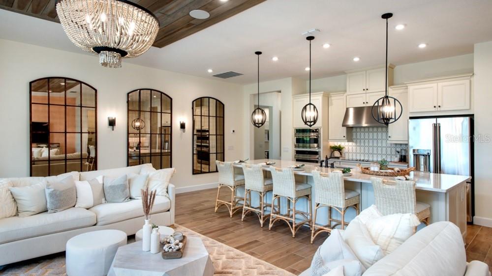An open-concept living room and kitchen featuring a large island, chandeliers, and arched wall mirrors — 5676 NEVIS TERRACE, KISSIMMEE, FL