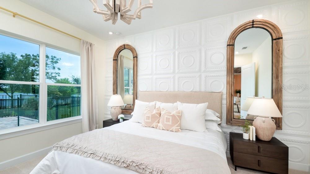 A bedroom features a bed with a textured wall, arched mirrors, and a lake view — 5676 NEVIS TERRACE, KISSIMMEE, FL