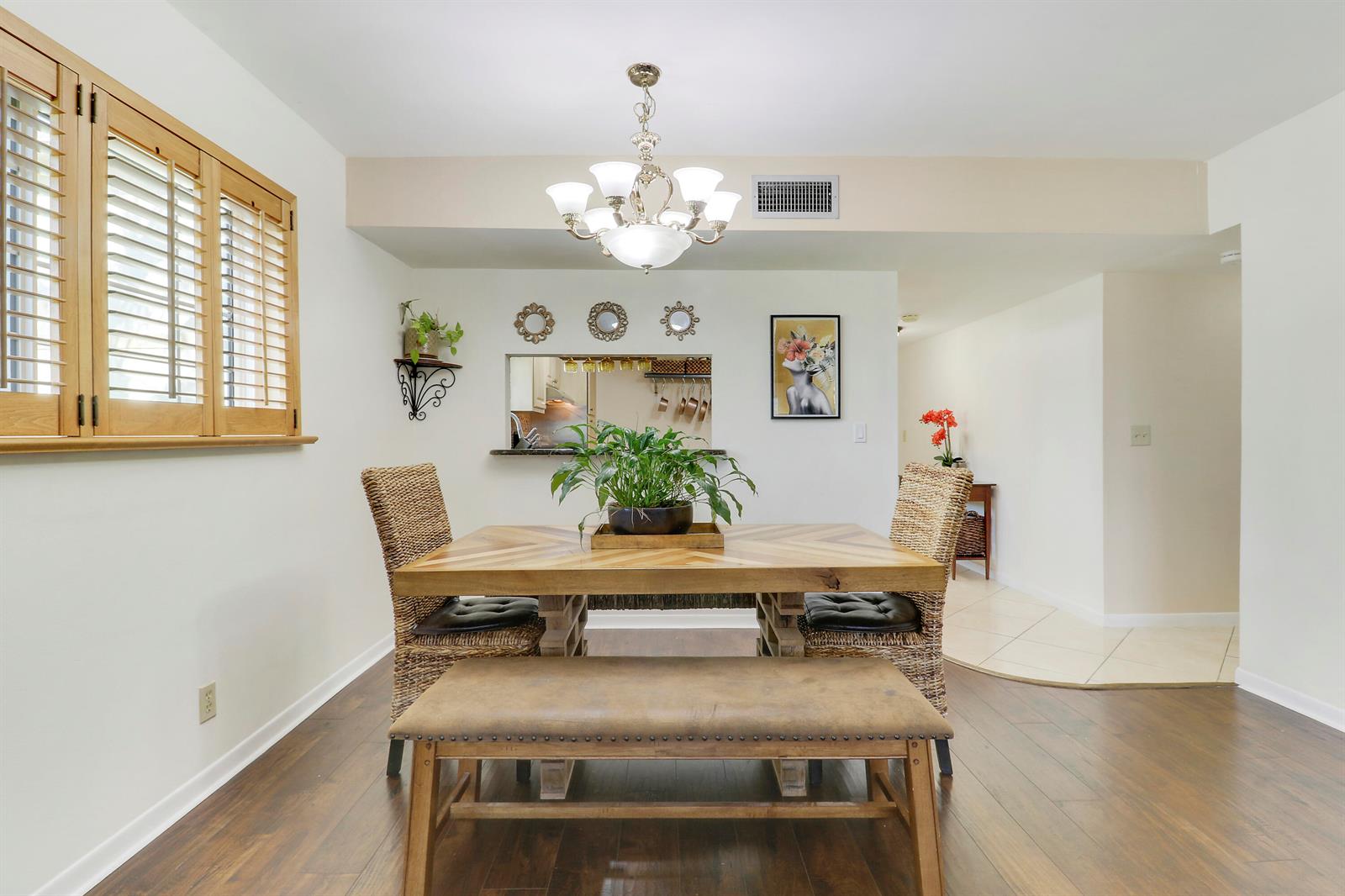 A dining room features a wooden table, woven chairs, a bench, and a chandelier — 1700 Dover Road # 106a, Delray Beach FL 33445, DELRAY BEACH, FL