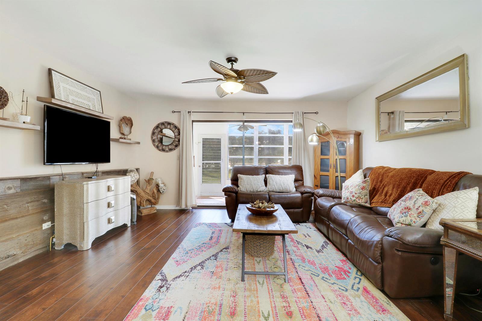 A living room features dark wood floors, a leather sofa, and a television on a dresser — 1700 Dover Road # 106a, Delray Beach FL 33445, DELRAY BEACH, FL