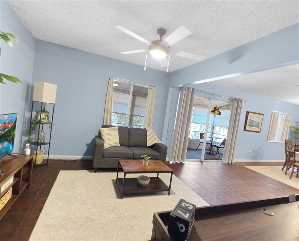 A living room with light blue walls, dark flooring, a gray sofa, and a ceiling fan — 553 FAIRWAYS CIRCLE UNIT B, OCALA, FL