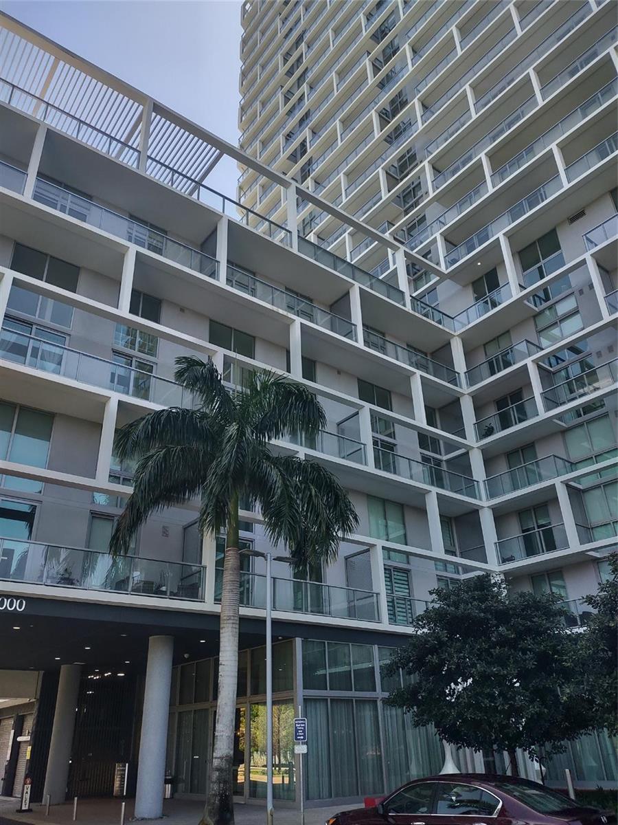 A low-angle exterior view of a modern multi-story apartment building with balconies and a palm tree — 2000 Metropica Way # 507, Sunrise FL 33323, SUNRISE, FL