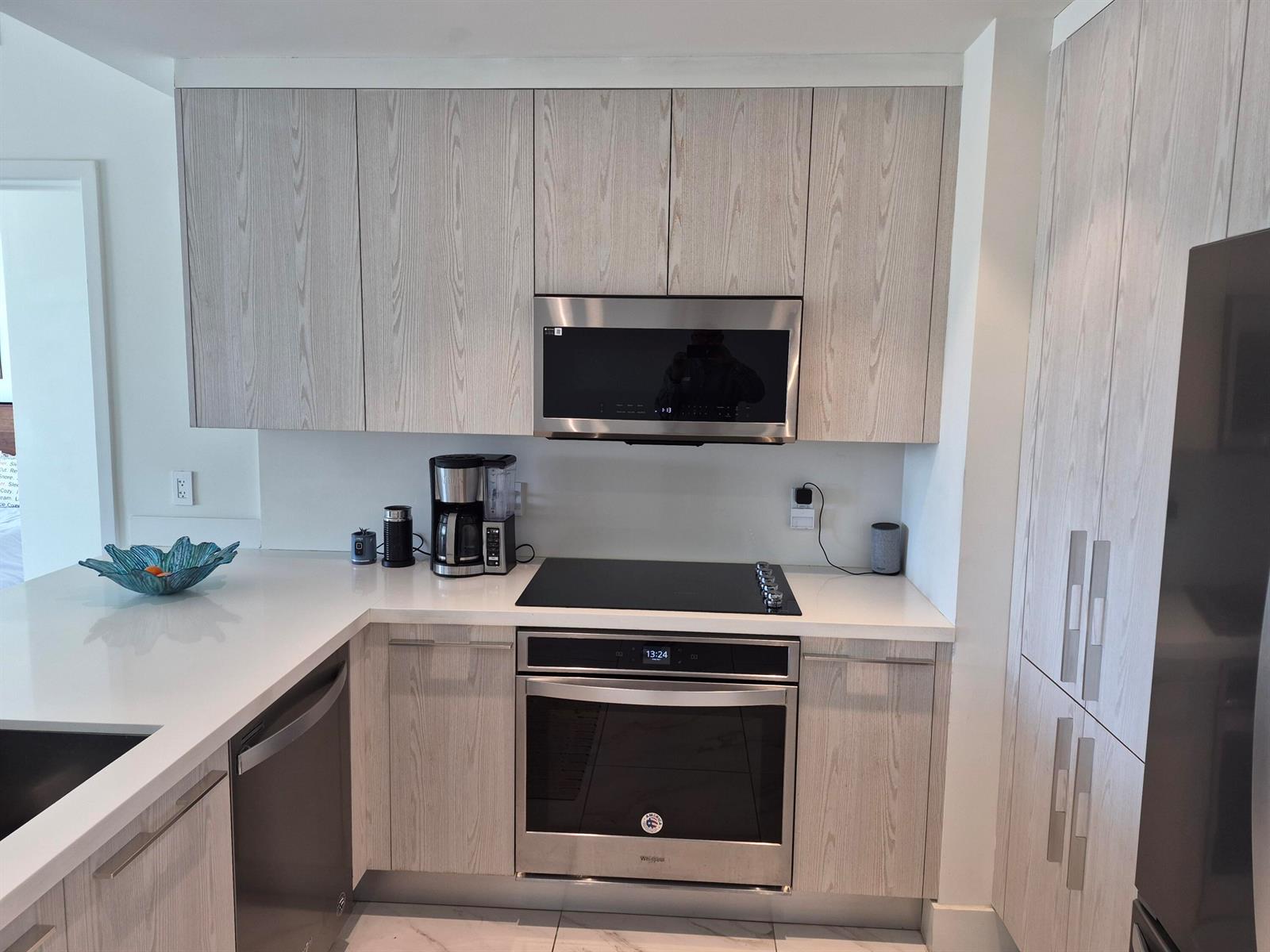 A modern kitchen features light wood-grain cabinets, stainless steel appliances, and white countertops — 2000 Metropica Way # 507, Sunrise FL 33323, SUNRISE, FL
