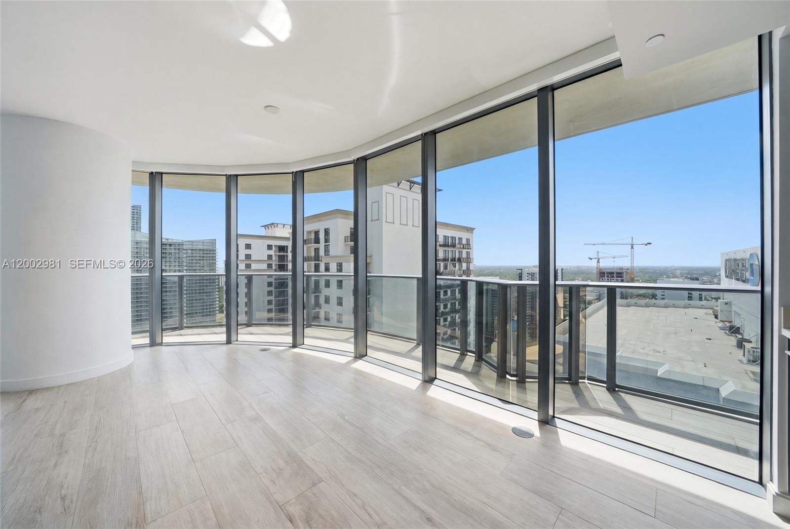 An empty room with light wood-look flooring and floor-to-ceiling windows overlooking a city skyline — 55 SW 9th St # 3106, Miami FL 33130, MIAMI, FL