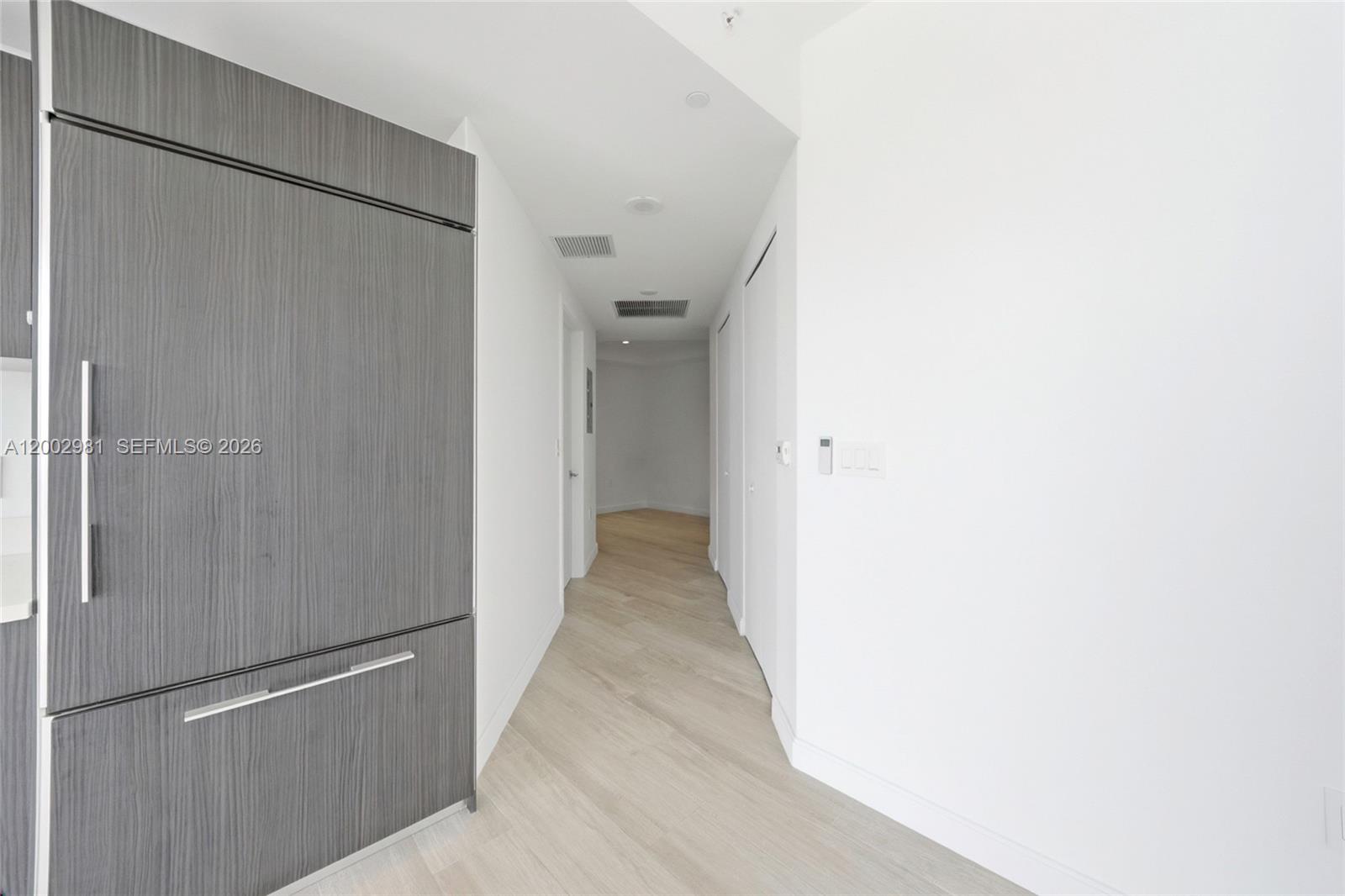 A hallway with light wood flooring leads to an open area past a gray refrigerator — 55 SW 9th St # 3106, Miami FL 33130, MIAMI, FL
