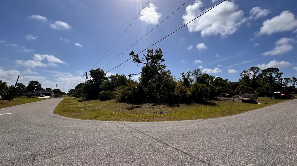 A vacant, grassy corner lot features scattered trees and shrubs under a bright blue sky — 116 AUSTRALIAN DRIVE, ROTONDA WEST, FL