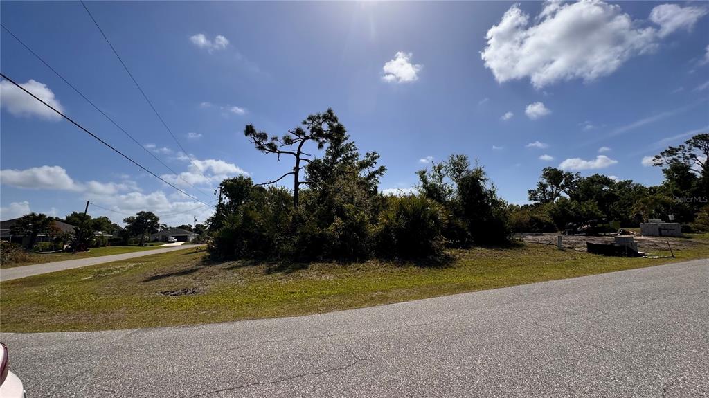 A vacant, grassy lot with trees and shrubs sits at the corner of two paved roads — 116 AUSTRALIAN DRIVE, ROTONDA WEST, FL