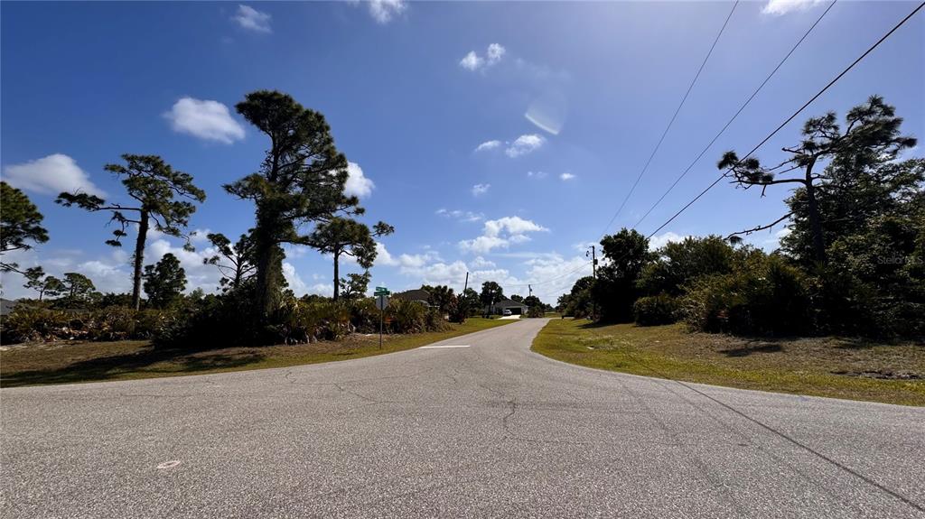 A paved road curves through a sunny, wooded residential area under a blue sky — 116 AUSTRALIAN DRIVE, ROTONDA WEST, FL