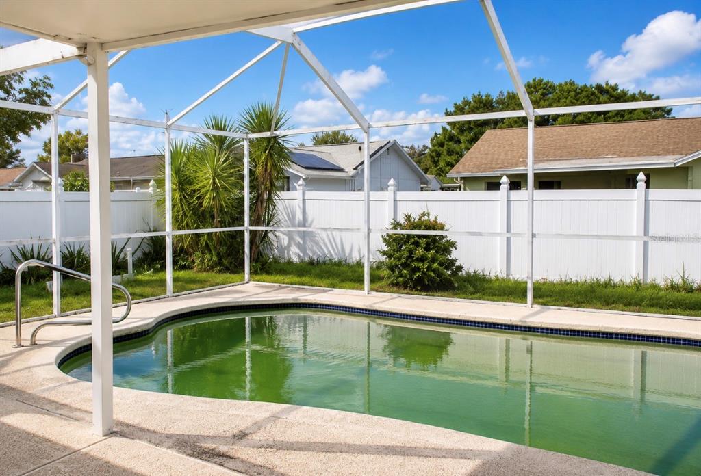 A backyard swimming pool with green water is enclosed by a white screen cage — 7717 MITCHELL RANCH ROAD, NEW PORT RICHEY, FL