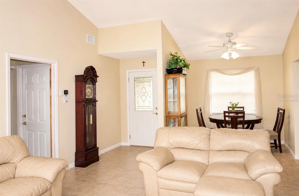 A living room with tile floors, a grandfather clock, and an adjacent dining area — 7717 MITCHELL RANCH ROAD, NEW PORT RICHEY, FL