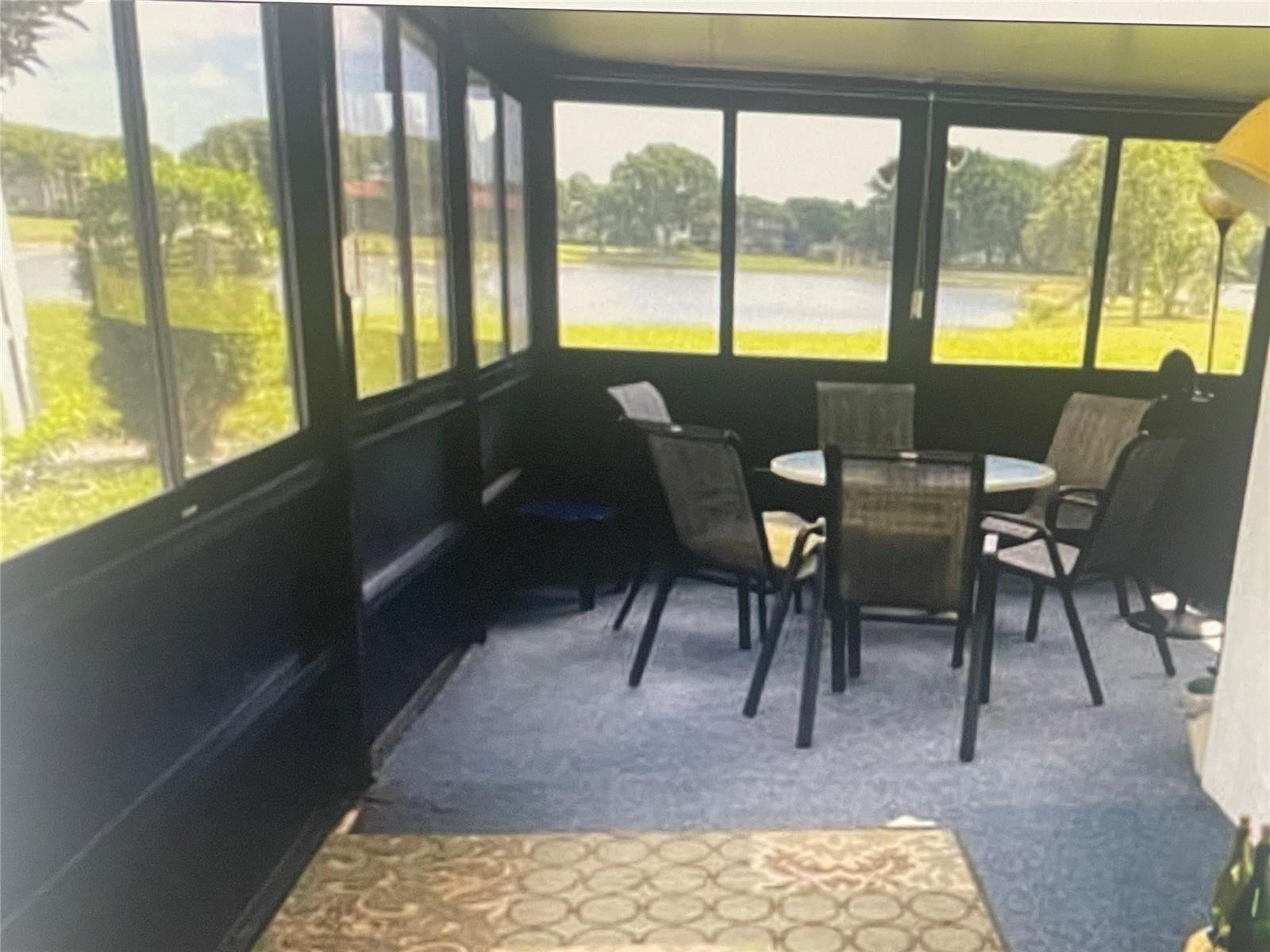 A sunroom with blue carpeting, a dining set, and large windows overlooking a lake — 5675 Northpointe Lane, Boynton Beach FL 33437, BOYNTON BEACH, FL