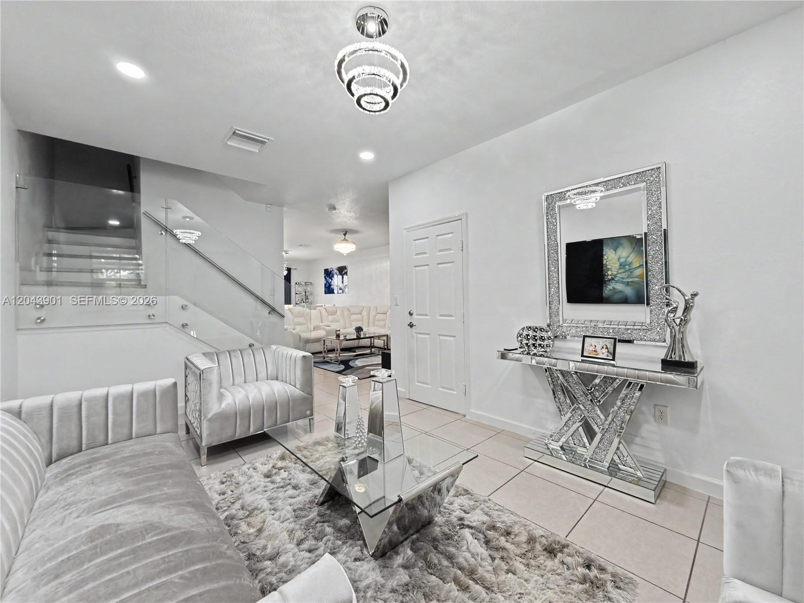 A modern living room features a glass staircase, mirrored furniture, and a shaggy area rug — 11611 SW 253rd St, Homestead FL 33032, HOMESTEAD, FL