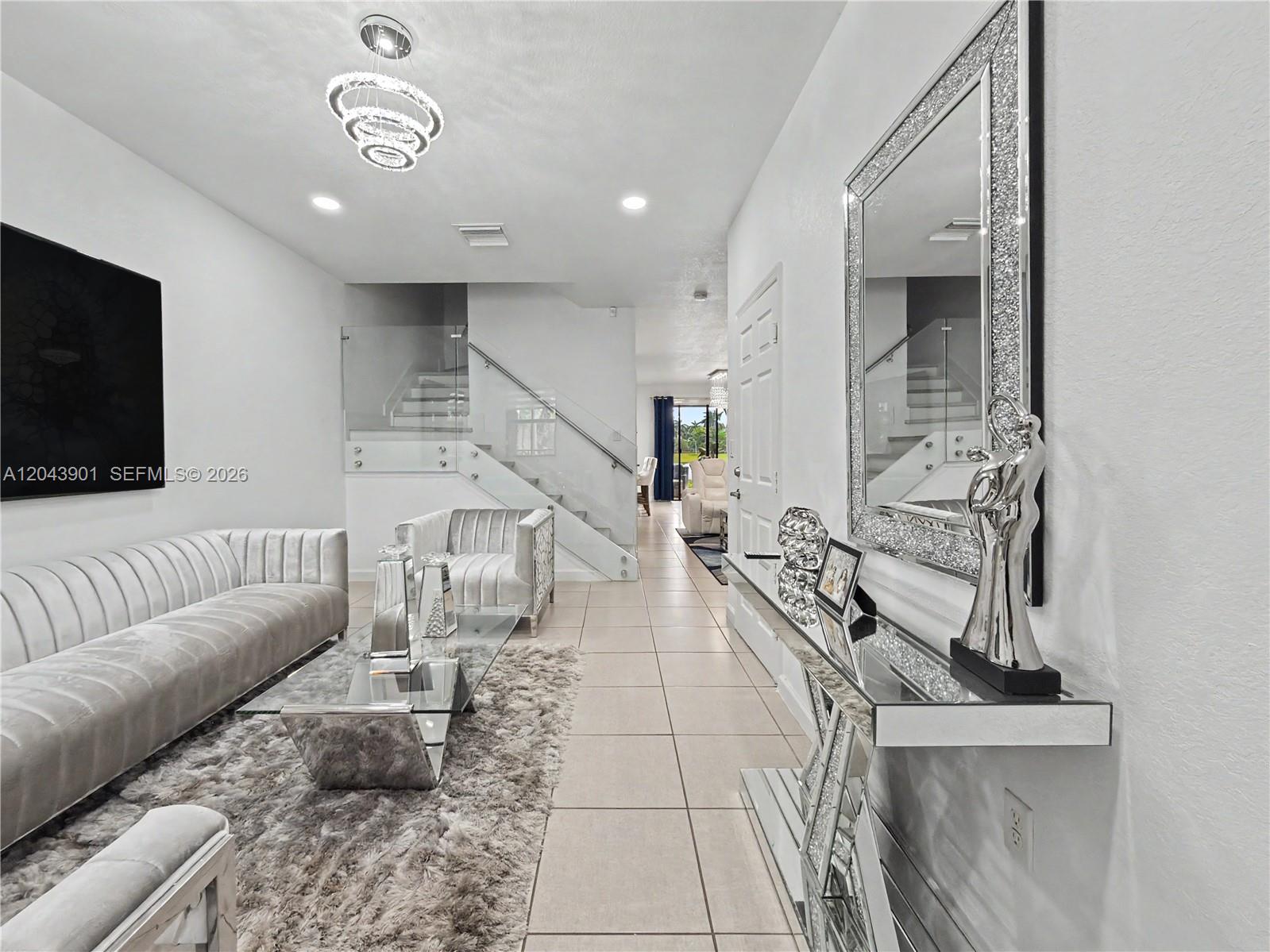 A modern living room features a glass staircase, mirrored console table, and light-colored tile flooring — 11611 SW 253rd St, Homestead FL 33032, HOMESTEAD, FL