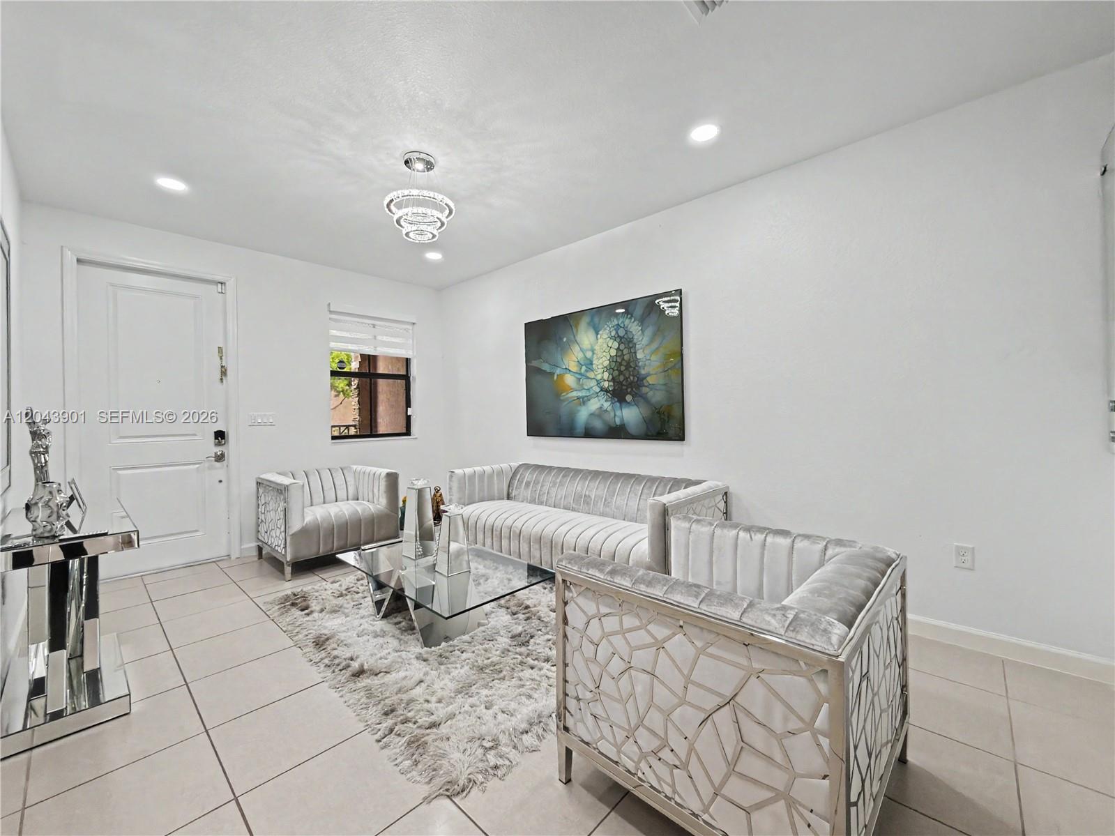 A modern living room features white walls, tiled floors, velvet furniture, and a glass coffee table — 11611 SW 253rd St, Homestead FL 33032, HOMESTEAD, FL