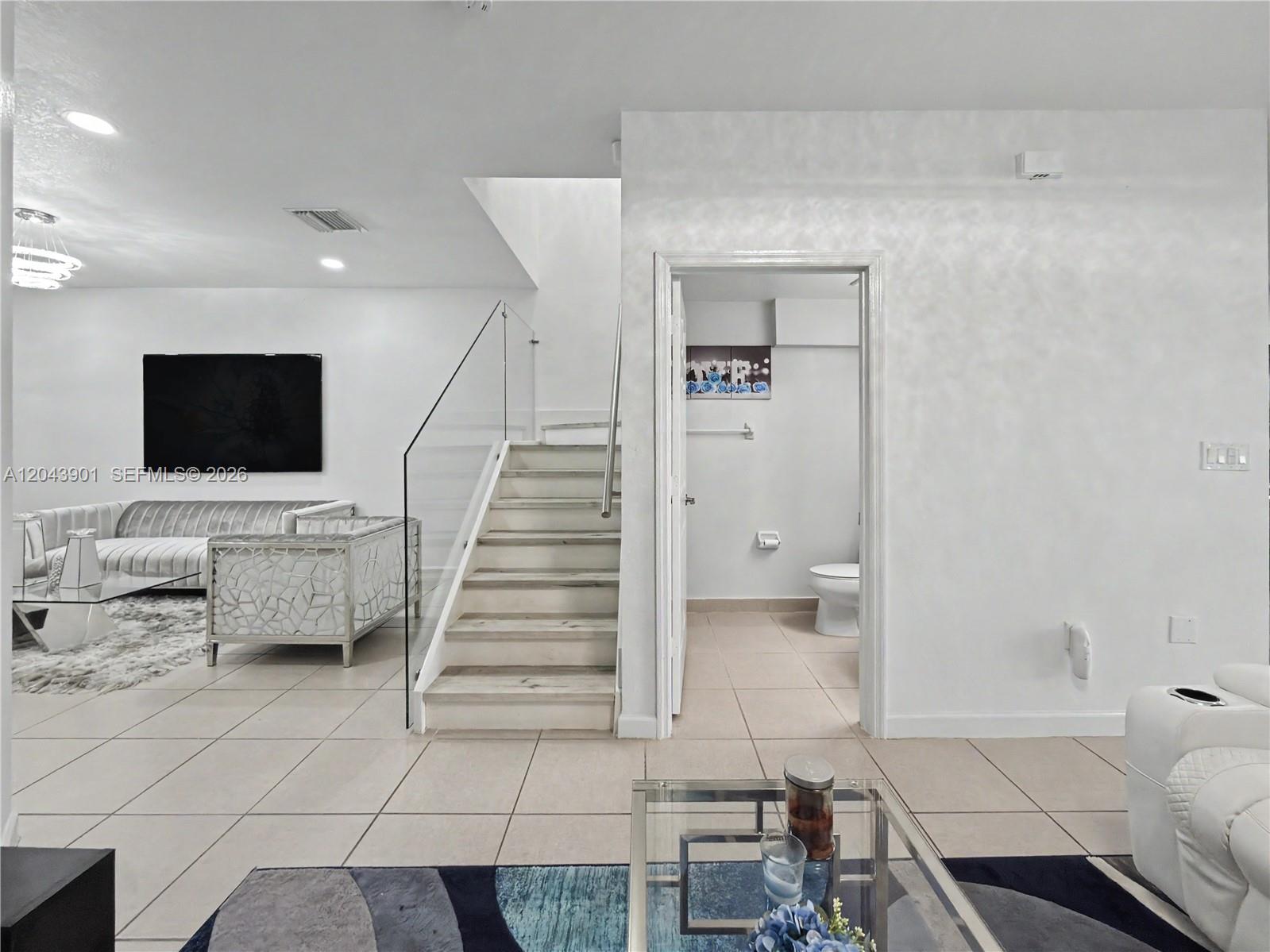 A living room features a glass-railed staircase and a doorway leading to a bathroom — 11611 SW 253rd St, Homestead FL 33032, HOMESTEAD, FL