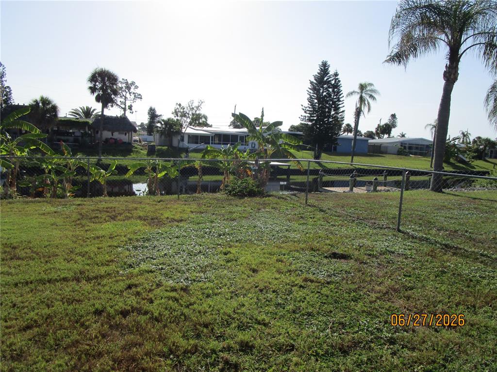 A grassy backyard features a chain-link fence overlooking a canal with neighboring houses beyond — 6344 MATARO COURT, NORTH PORT, FL