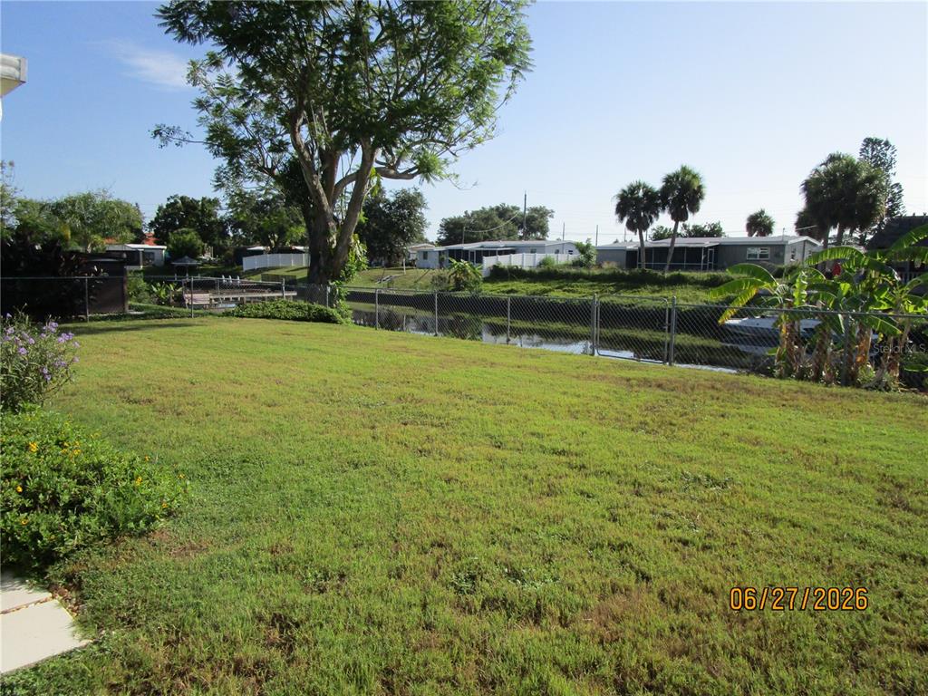 A grassy backyard features a large tree, a chain-link fence, and a canal view — 6344 MATARO COURT, NORTH PORT, FL