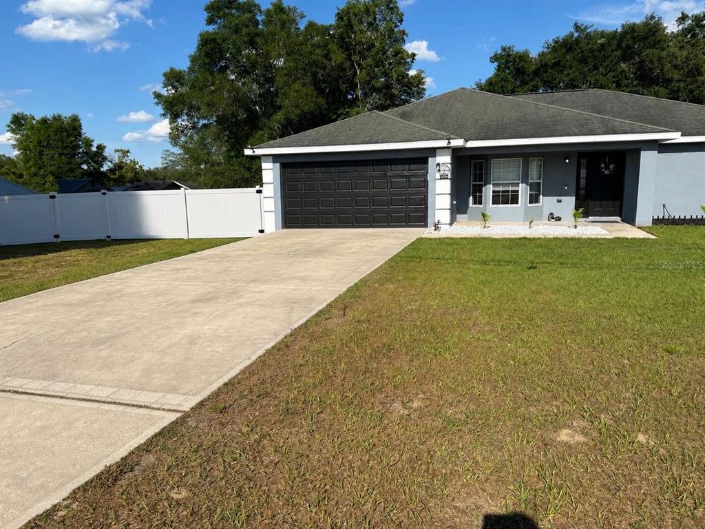 A single-story house with a gray exterior, dark garage door, and a white vinyl fence — 15759 SE 97TH AVENUE, SUMMERFIELD, FL