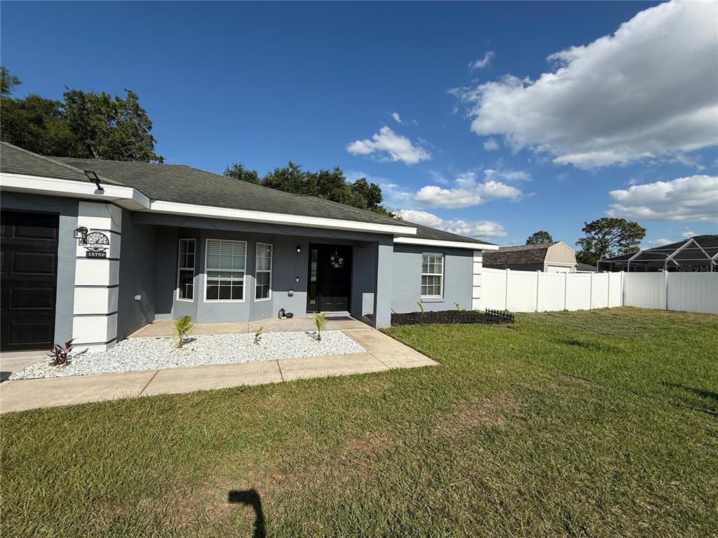 A gray single-story house features a white-rock garden bed, a front walkway, and white fencing — 15759 SE 97TH AVENUE, SUMMERFIELD, FL