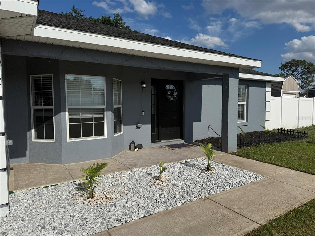 A gray house exterior features a covered porch, white rock landscaping, and a dark door — 15759 SE 97TH AVENUE, SUMMERFIELD, FL