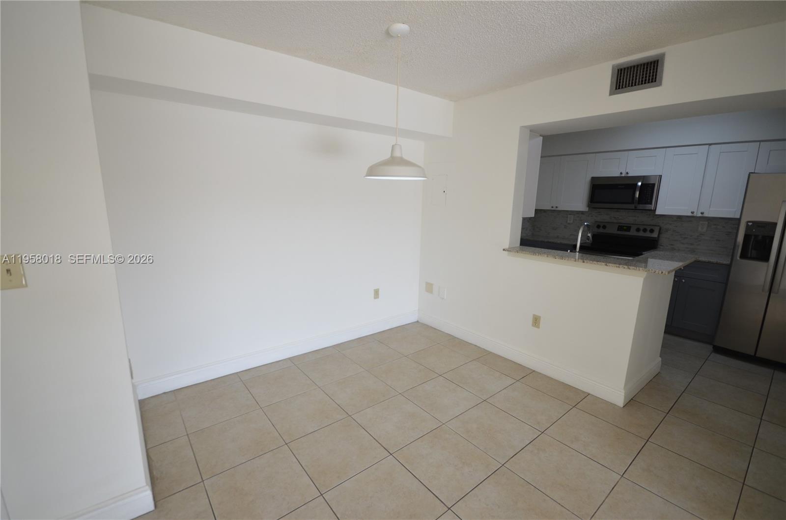 An empty dining area with tile flooring and a pendant light overlooks a kitchen — 15201 SW 80th St # 207, Miami FL 33193, MIAMI, FL