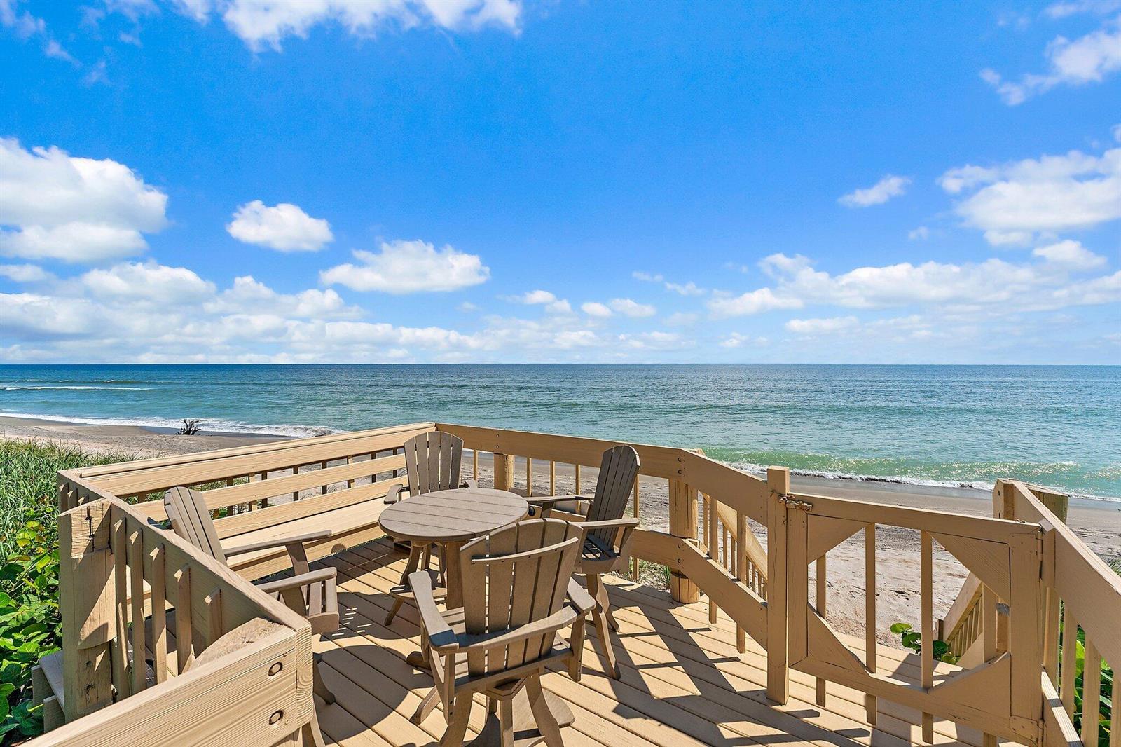 A wooden deck with patio furniture overlooks the ocean and a sandy beach — 19900 Beach Road # 201, Jupiter FL 33469, JUPITER, FL