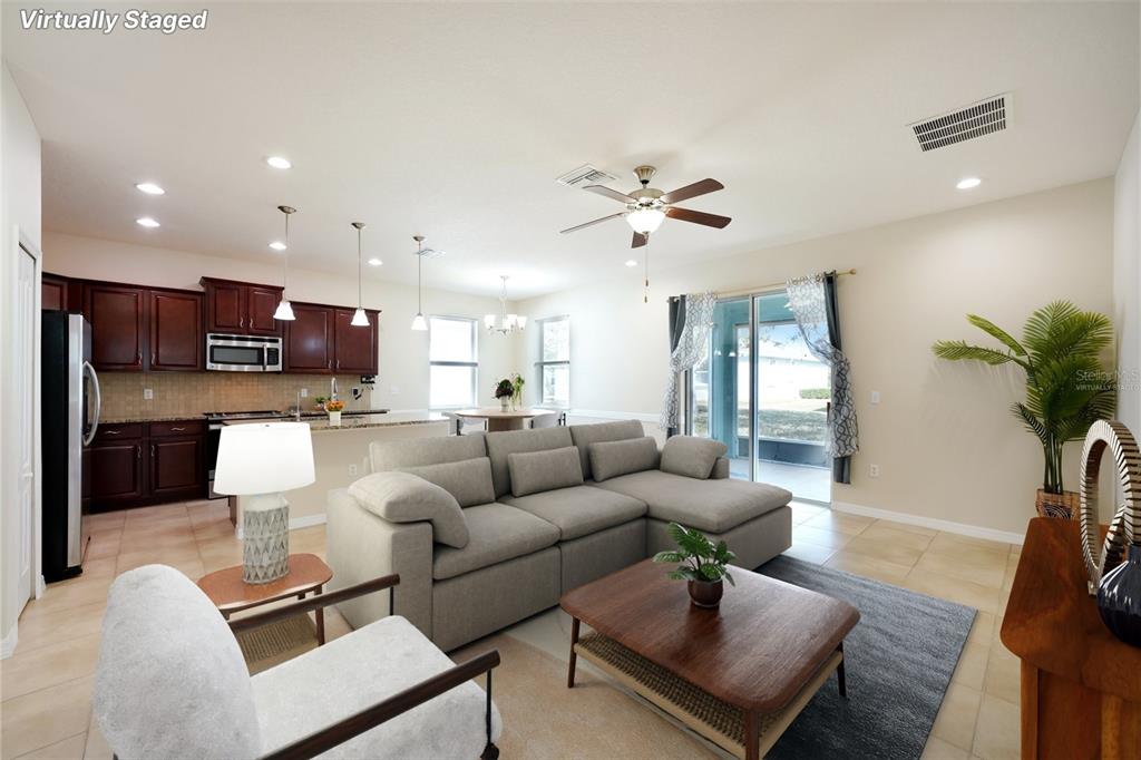 This open-concept living room features a sectional sofa, kitchen with dark cabinets, and tile flooring — 11129 KISKADEE CIRCLE, NEW PORT RICHEY, FL