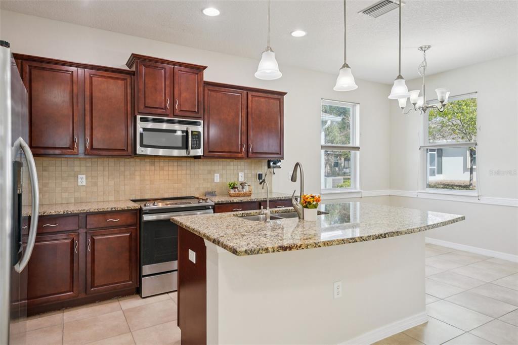 A kitchen with dark wood cabinets, granite countertops, a center island, and stainless steel appliances — 11129 KISKADEE CIRCLE, NEW PORT RICHEY, FL